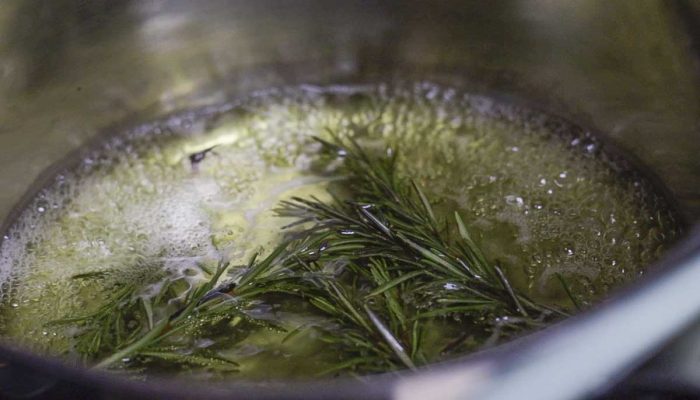 water and rosemary sprigs simmering in a saucepan
