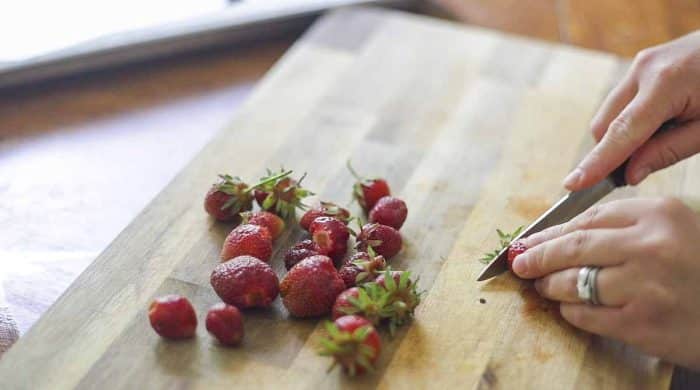 slicing strawberries on a wood countertop with a pairing knife