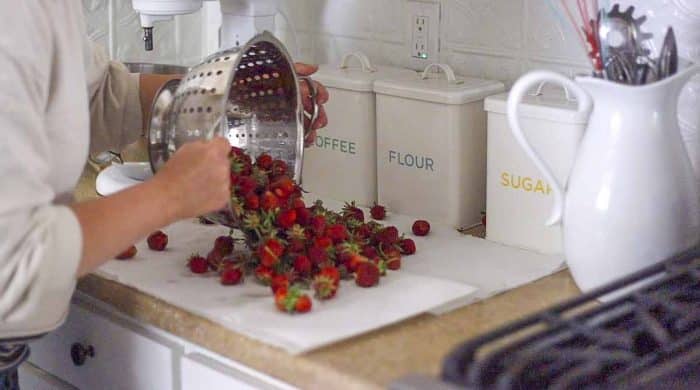 pouring strawberries in a strainer onto a countertop covered in paper towel