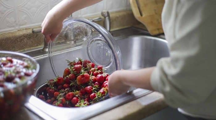 pouring strawberries into a stainer in a sink