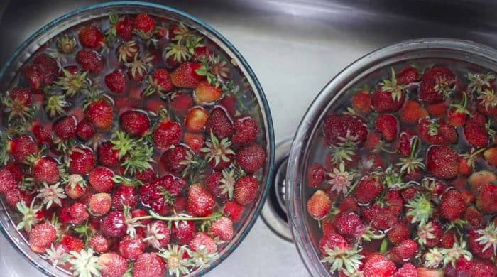 two bowls of strawberries soaking in water and vinegar in a sink