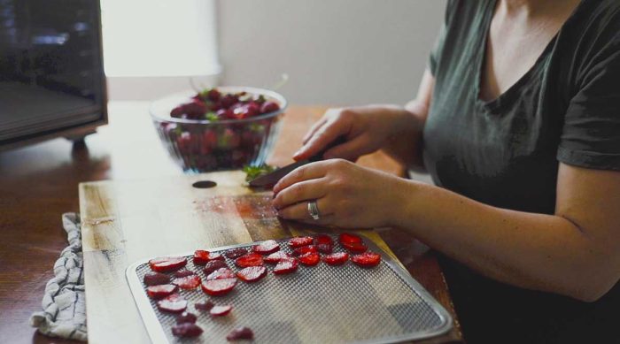 woman slicing strawberries and placing them on a dehydrator pan.