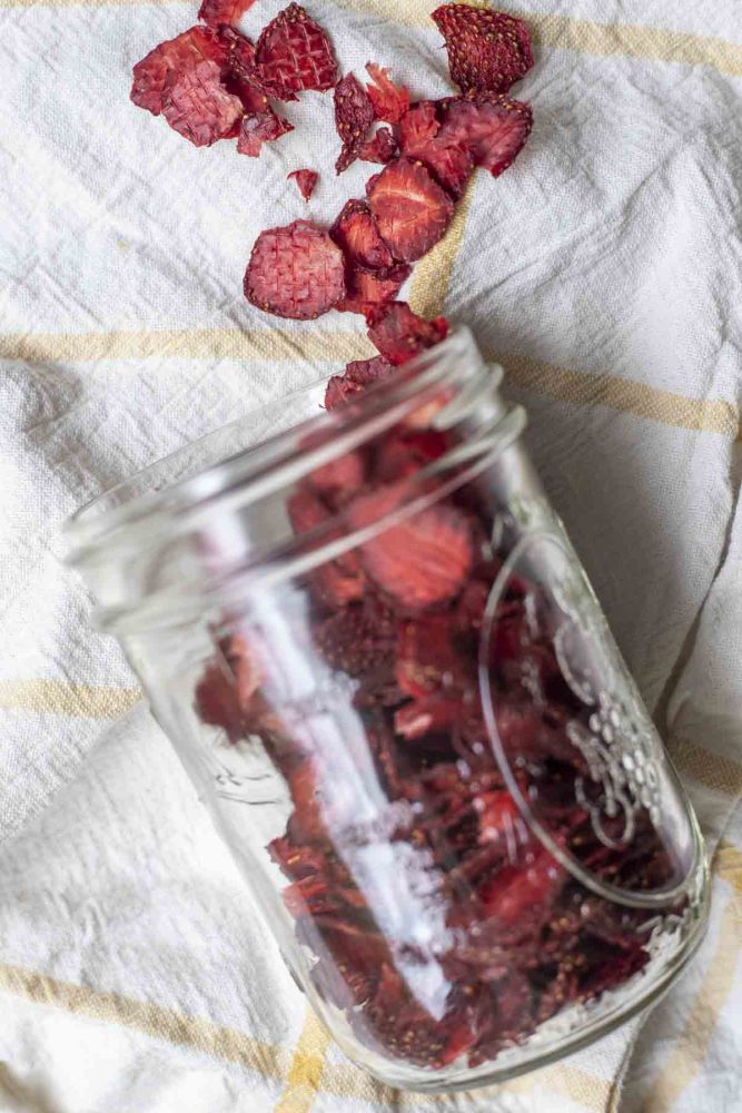overhead photo of dried strawberries in a mason jar tipped over and sprinkled out on a white and yellow towel