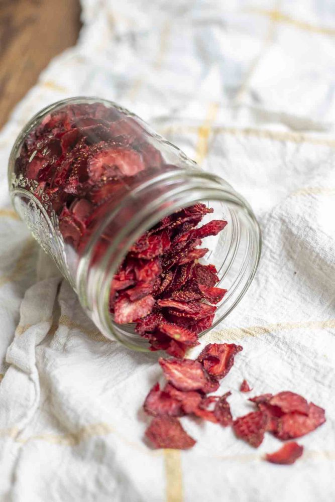 dehydrated strawberries in a mason jar tipped over and spilling out on a white and yellow checked towel