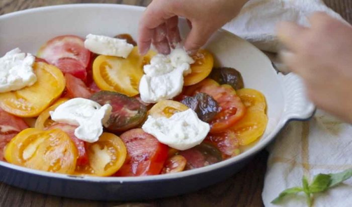 placing burrata cheese on top of sliced tomatoes in a baking dish