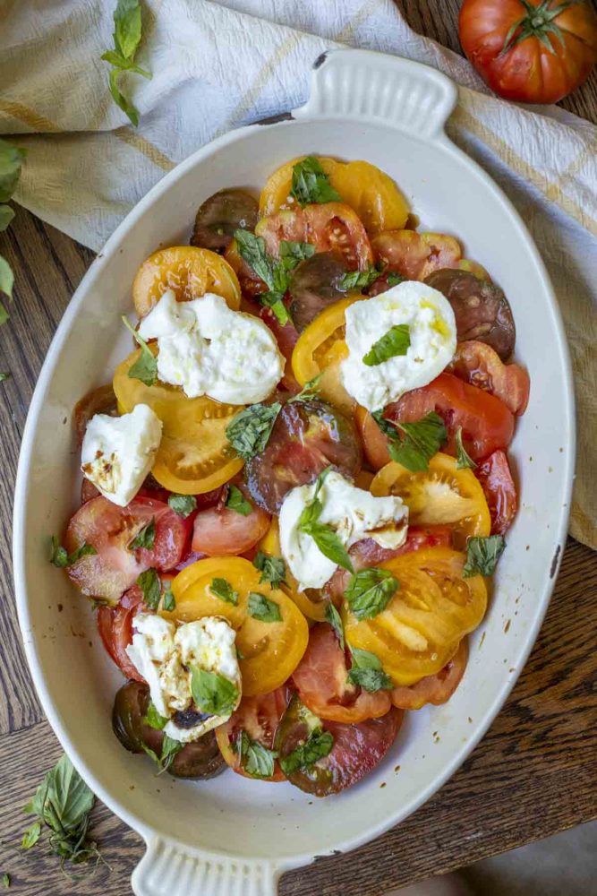 overhead photo of a burrata capers salad with fresh heirloom tomatoes sliced, burrata cheese, and fresh basil topped with olive oil and balsamic vinegar