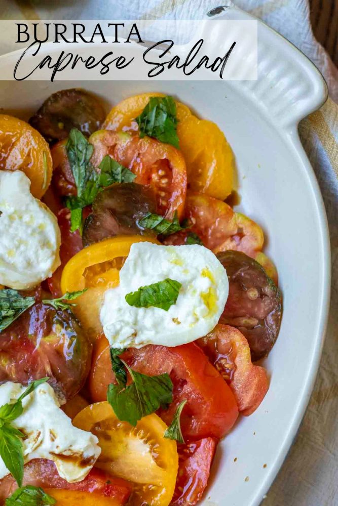 a white baking dish with fresh sliced tomatoes, burrata cheese, fresh basil and topped with olive oil and balsamic vinegar.