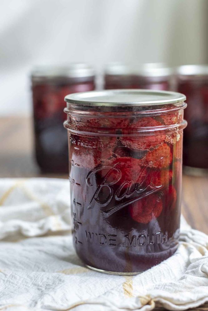 a jar of canned strawberries in syrup on a white and yellow towel with more jars in the background