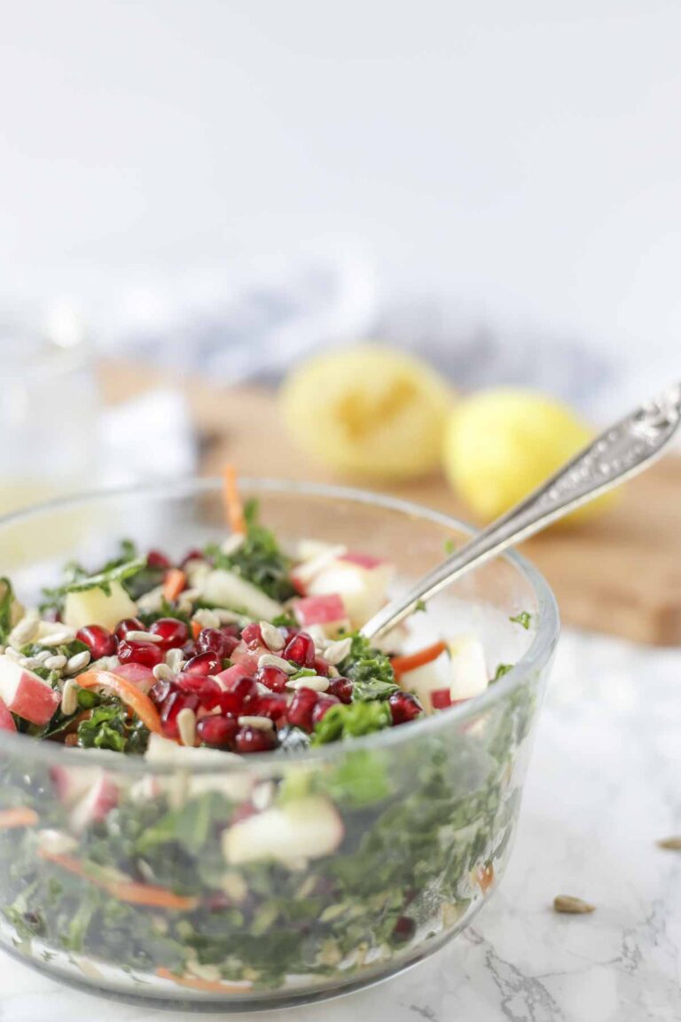 Glass bowl with a kale apple salad topped with pomegranate seeds.