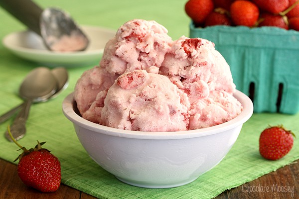 strawberry ice cream in a white bowl on a green towel with a container of strawberries in the background