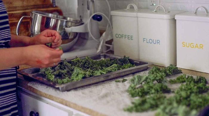 hands ripping kale up and placing it on a stainless baking sheet