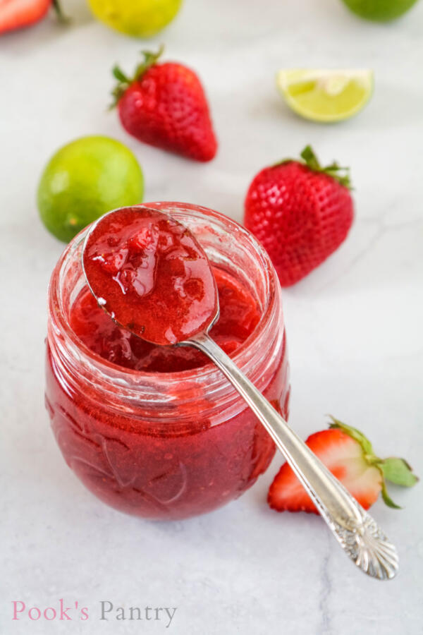 strawberry key lime jam in a jar with a spoonful of jam balancing on the rim