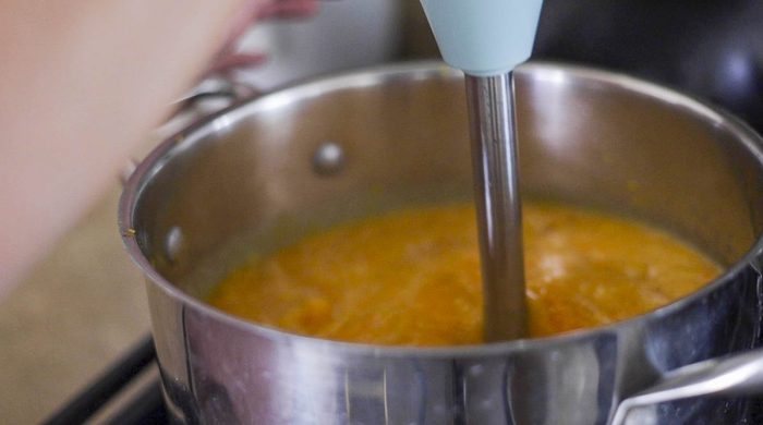 an immersion blender in a  pot full of butternut squash and broth