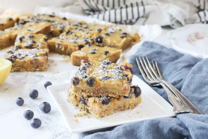 blueberry lemon bars stacked on a white plate with more dessert bars behind them