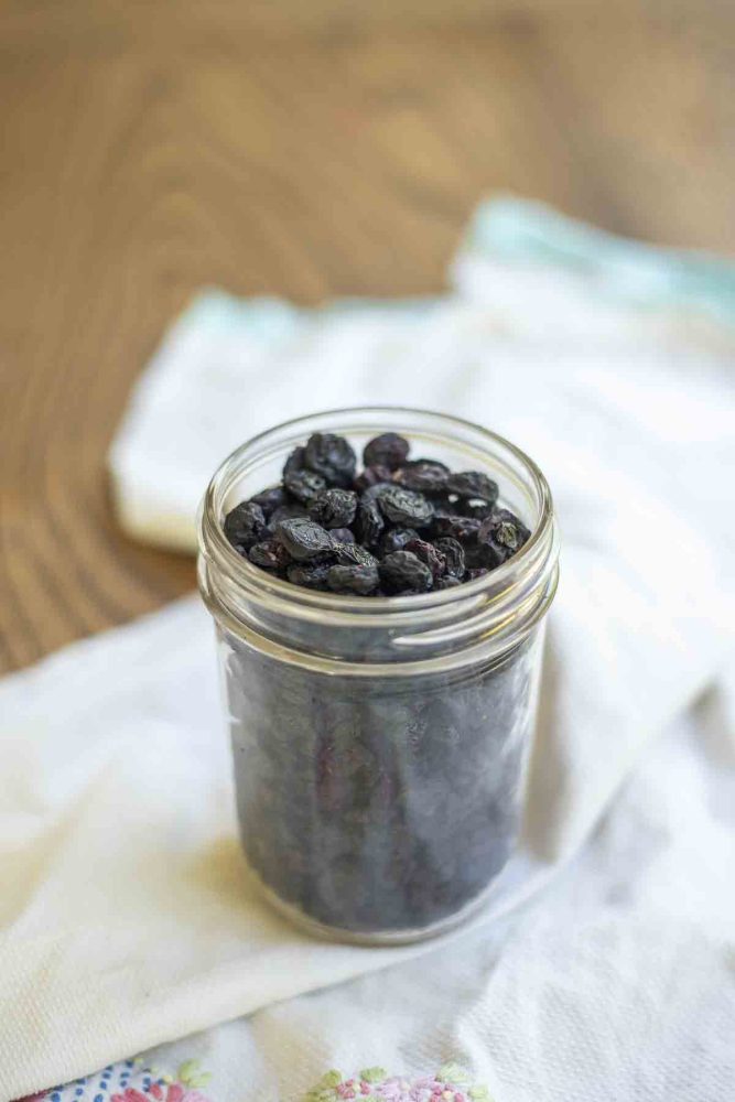 jar of dehydrated blueberries on a white and teal towel on a wood table