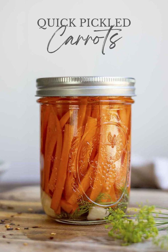 pickled carrots in a glass jar with a lid on a wood cutting board with dill and red pepper flakes