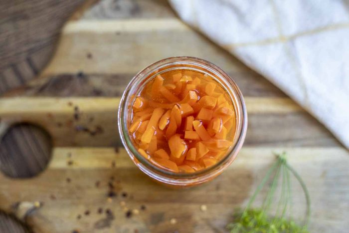 overhead photo of quick pickled carrot sticks in a jar. The jar is on a wood cutting board with ingredients spread around.