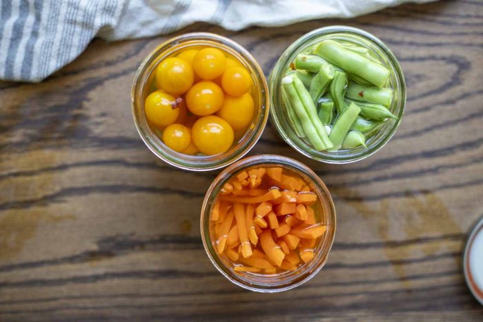 three jars of quick pickled carrots, green beans and tomatoes on a wood table