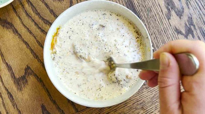 fork mixing a bowl of oats, milk, and other ingredients on a wood countertop