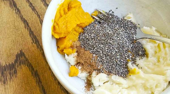 mashed banana, pumpkin puree, chia seeds and pumpkin spice in a white bowl on a wood countertop