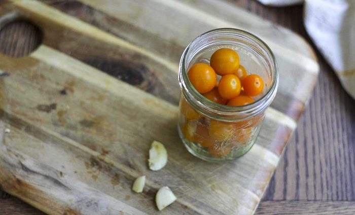 cherry tomatoes added to a mason jar on a wood cutting board with garlic surrounding the jar.