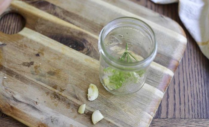 adding dill and garlic to a mason jar on a cutting board