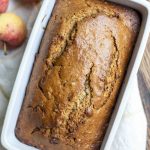 overhead photo of sourdough cinnamon apple bread on a white and yellow towel with apples on top