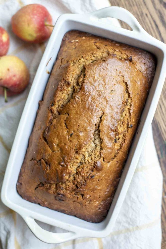 overhead photo of sourdough cinnamon apple bread on a white and yellow towel with apples on top