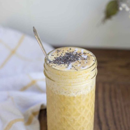 pumpkin spice smoothie topped with chia seeds in a glass jar with a spoon in the jar. A white and yellow towel is in the background