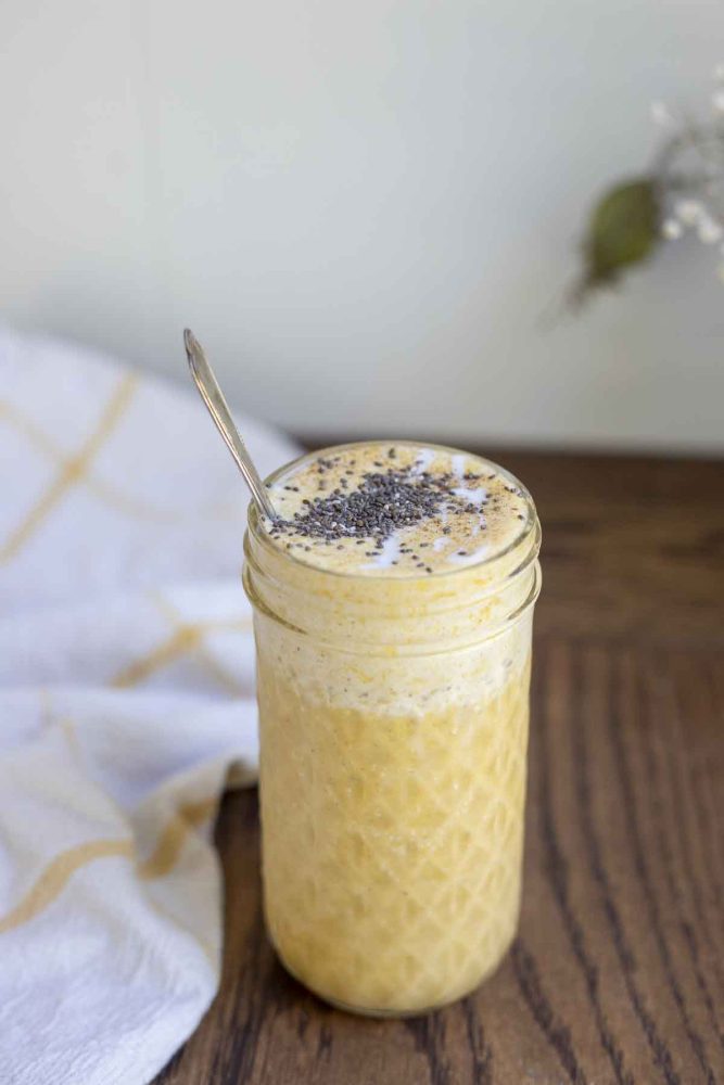 pumpkin spice smoothie topped with chia seeds in a glass jar with a spoon in the jar. A white and yellow towel is in the background