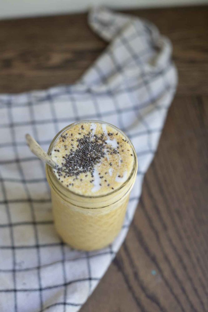 photo of pumpkin spice smoothie topped with chia seeds and yogurt in a glass jar on a black and white checked towel
