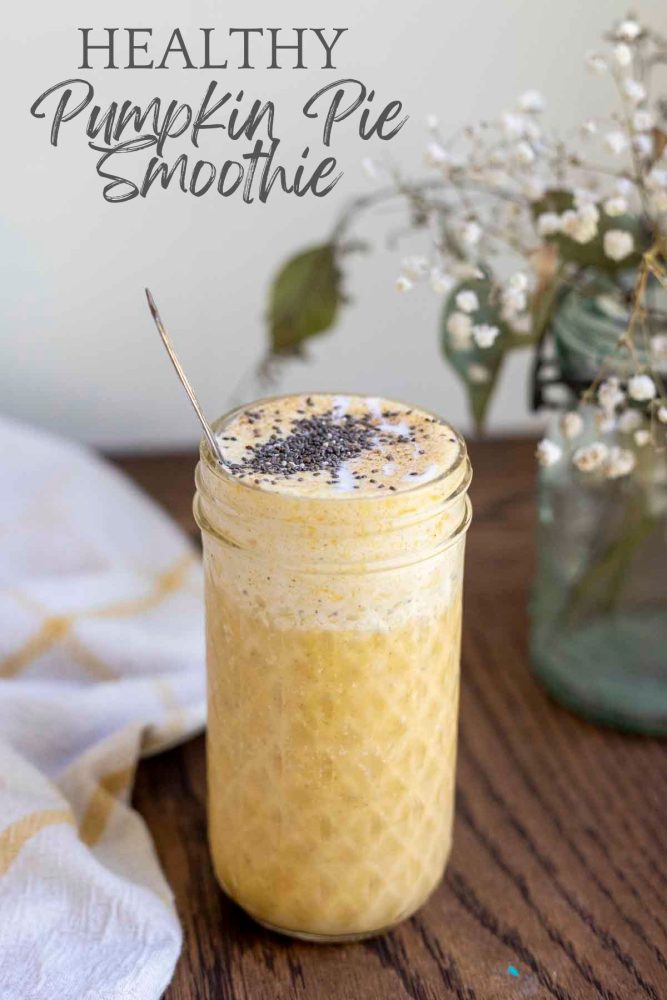 healthy pumpkin spice smoothie in a glass jar on a wood countertop with a yellow and white towel and a jar of flowers in the background