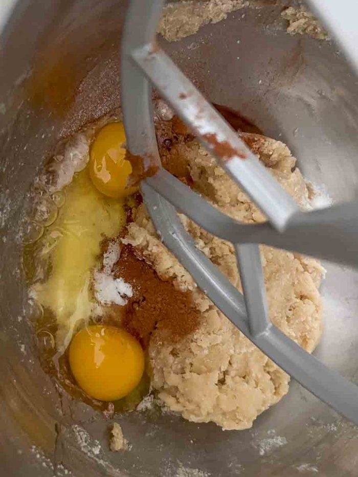 eggs, cinnamon, baking soda and baking powder adding to fermented dough in a stand mixer bowl with paddle attachment