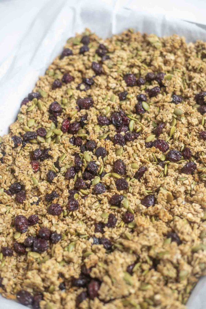 parchment lined sheet pan with pumpkin spice granola with pumpkin seeds and dried cranberries