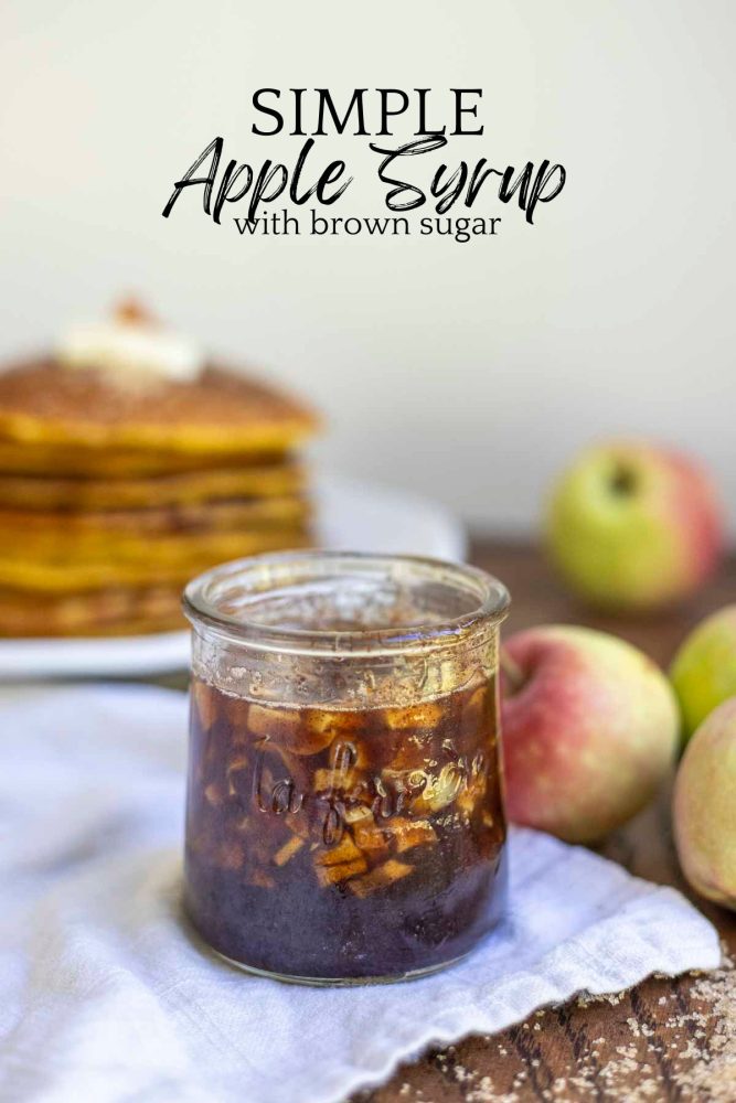 apple syrup made with brown sugar and apples in a small jar on a napkin with pancakes and apples in the background