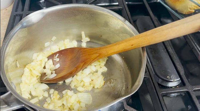 onions sautéing in a pot with a wooden spoon in the pot