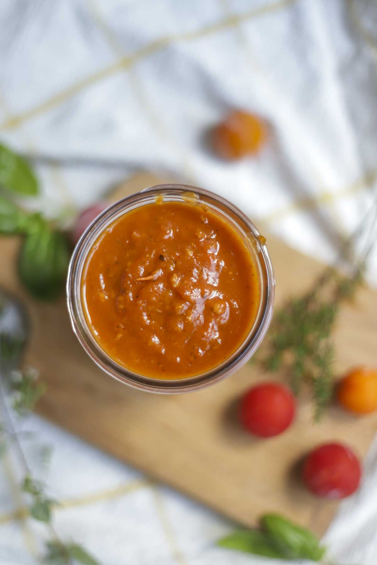 overhead photo of a jar of cherry tomatoes on a wood cutting board with fresh herbs and cherry tomatoes on the board. 