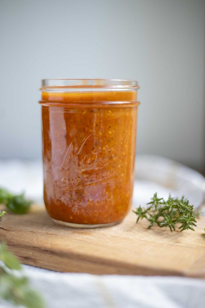 cherry tomato sauce in a mason jar on a wooden cutting board with fresh herbs on the cutting board