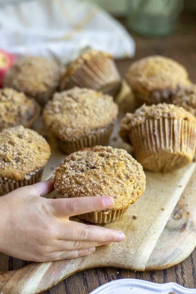 hand grabbing a sourdough apple muffin off of a cutting board with more muffins
