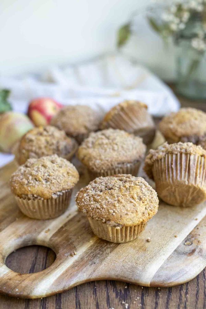 sourdough apples muffins scattered on a wood cutting board with a towel and eucalyptus in the background
