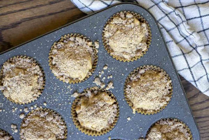 sourdough apple muffins topped with crumble topping in a muffin tin with a white and black towel to the right