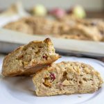 two apple sourdough scones stacked on a white plate with a baking dish of more scones in the background