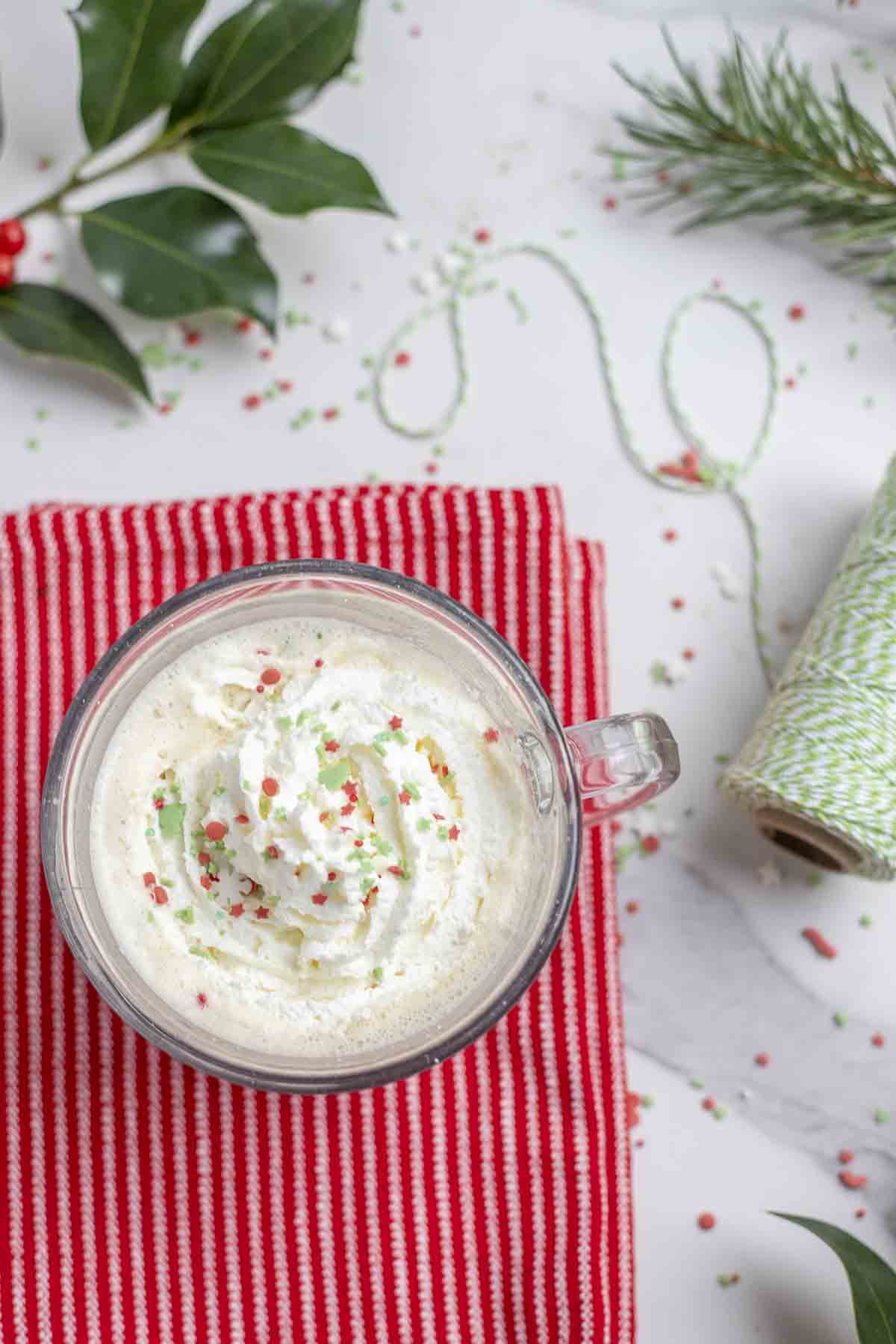 eggnog latte topped with whipped cream and sprinkles on a red stripped towel.