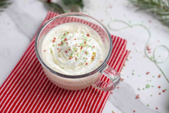 eggnog latte in a glass mug topped with whipped cream and Christmas sprinkles on a red towel 