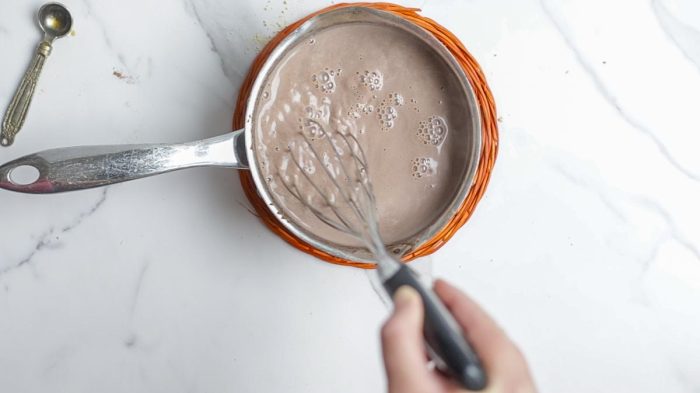 whisking hot cocoa together in a small saucepan on a orange pot holder