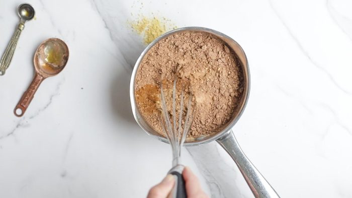 whisking hot chocolate ingredients together in a small saucepan on a white countertop