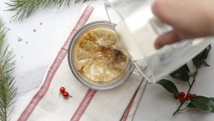 pour eggnog over coffee in a mug on a cream and red stripped towel.