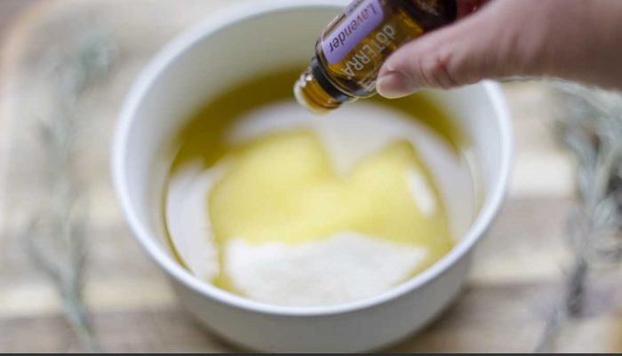 essential oil being dripped into a bowl of oil and sugar on a wood cutting board 