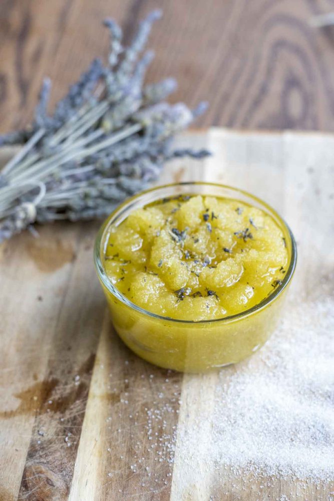 sugar scrub with lavender essential oil on a wood cutting board with a bundle of lavender behind the jar