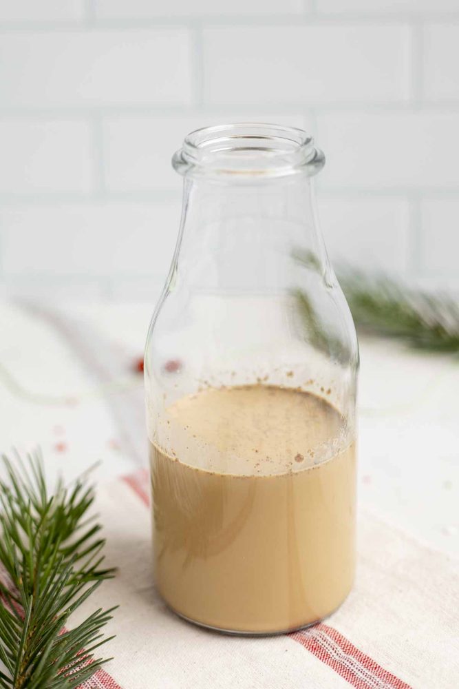 gingerbread coffee creamer in a glass bottle on a white and red stripped towel with greenery to the left